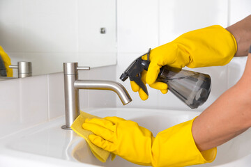 Yellow gloves cleaning sink in the bathroom. Disinfecting the bathroom. Prevention of coronavirus infection.