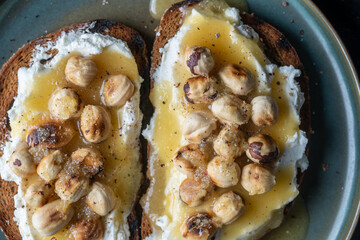 Two bread toast with cream cheese, roasted hazelnuts, honey, pepper and salt, close up, top view