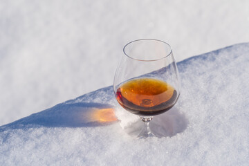 Glass of cognac on a bed of snow and white background, close up