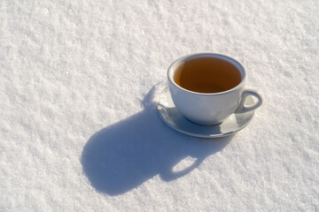 White cup of hot tea on a bed of snow and white background, close up