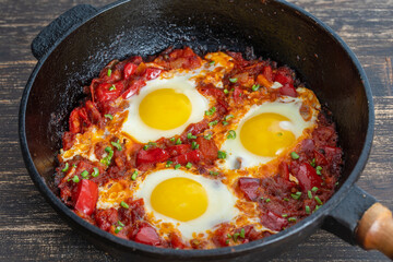 Shakshuka, fried eggs with tomatoes, onion, red pepper and spices in cast iron pan