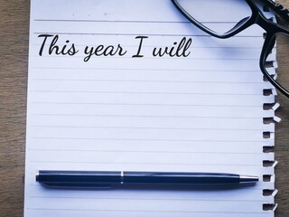 Phrase This year i will written on a piece of paper with a pen an eye glasses. Motivational quote.