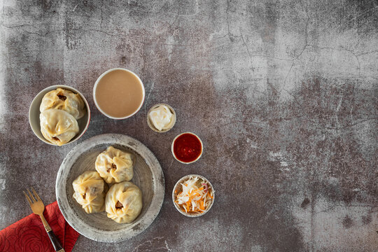 Buuza in a plate, around her sauce-seasoning of tomatoes with garlic, sour cream, fermented cabbage with carrots, a bowl of green tea with milk. Vintage fork on a red napkin. Copy space, top view.
