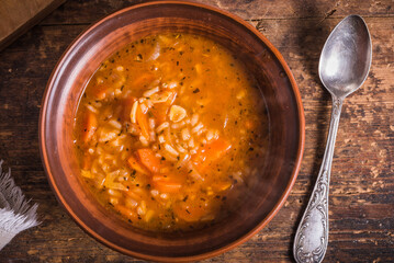 Vegetarian rice tomato soup in a clay bowl and spoon, on a rustic wooden table, top view - healthy rustic lunch