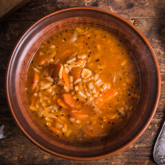 Vegetarian rice tomato soup in a clay bowl and spoon, on a rustic wooden table, top view - healthy rustic lunch