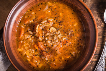 Vegetarian rice tomato soup in a clay bowl and spoon, on a rustic wooden table, top view - healthy rustic lunch