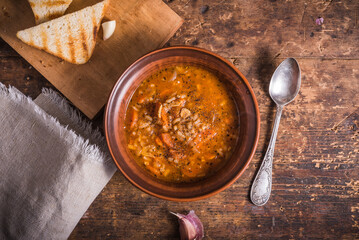 Vegetarian rice tomato soup in a clay bowl and spoon, on a rustic wooden table, top view - healthy rustic lunch