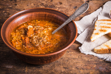 Vegetarian rice tomato soup in a clay bowl and spoon, on a rustic wooden table with toast - a healthy italian country lunch