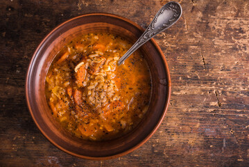 Vegetarian rice tomato soup in a clay bowl and spoon, on a rustic wooden table, top view, copy space - healthy Italian rustic lunch