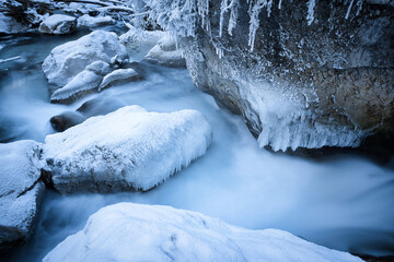 snow covered rocks in a river captured as smooth long exposure; winter landscape