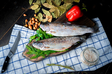Two raw rainbow trout with garnish on a wooden board. 
