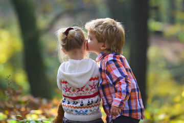 Brother kiss sister with love in woods. Little boy kiss small girl friend in autumn forest. Valentines day concept. Childhood friendship and children early development.