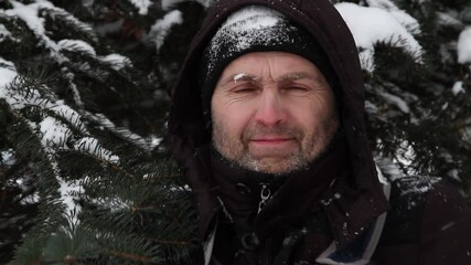 Portrait of a freezing and contented man against the background of snow-covered branches of a Christmas tree. - Powered by Adobe