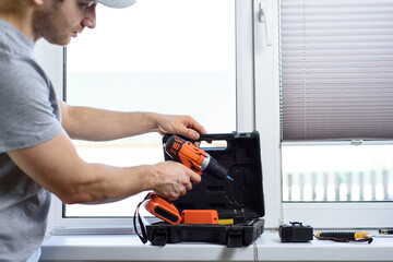 Man installing gray pleated blinds on the window with screwdriver