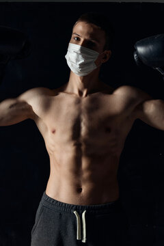 athlete in a medical mask and boxing gloves on a black background pumped up torso