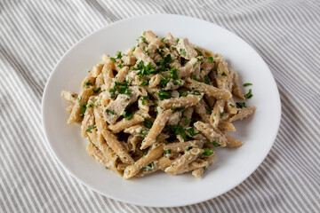 Homemade Chicken Alfredo Penne with Parsley on a white plate, low angle view.