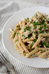 Homemade Chicken Alfredo Penne with Parsley on a white plate, side view.