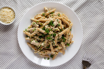 Homemade Chicken Alfredo Penne with Parsley on a white plate, top view. Overhead, from above, flat lay.