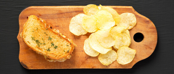 Homemade French Onion Melt Cheese Sandwich with Chips on a rustic wooden board on a black surface, top view. Flat lay, overhead, from above.