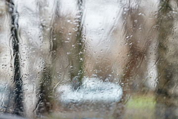 Rain drops on the window. Abstract city background with white car and trees