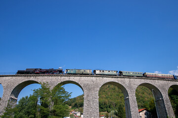 Old steam train leaving the railway station of Tolmin, Slovenia stone bridge