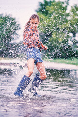 Teenage girl in boots stands in a large puddle and makes a lot of splashes of water