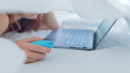 A woman lies in bed holding a clitoral vibrator and watching porn on a laptop. The girl has sex...