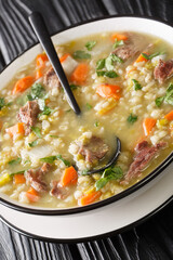 Scotch broth is a traditional Scottish soup made from lamb, and vegetables, barley, peas closeup in the plate on the table. Vertical