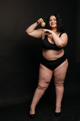 Obraz premium Plus size model in lingerie, fat sexy woman in underwear on black studio background, body positive concept, full length portrait,a beautiful plus size model holds an apple in her hand