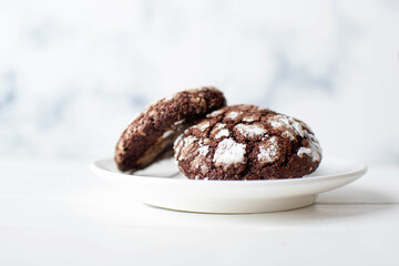 Close up of freshly baked chocolate cookies on white saucer over rustic wooden background. 