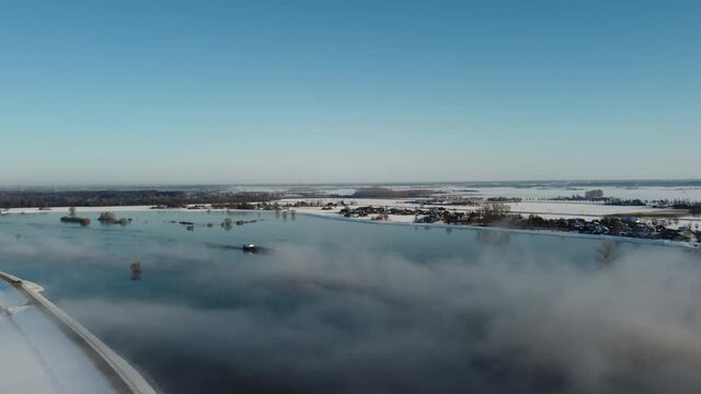 Ship sailing into the fog over the river Ijssel with ice and snow during a cold winter day in The Netherlands. Aerial drone point of view.
