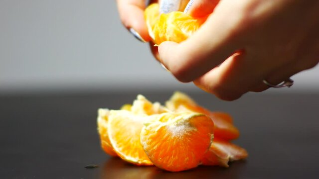 Woman's hands in beautiful nail polish splits mandarin into slice with blurred background