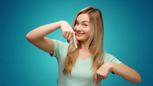 Young woman pointing fingers down, showing copy space, against blue background - Powered by Adobe
