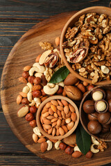 Tray with bowls with different nuts on wooden background