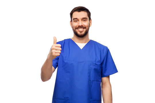 Healthcare, Profession And Medicine Concept - Happy Smiling Doctor Or Male Nurse In Blue Uniform Showing Thumbs Up Over White Background