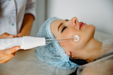 Receiving electric d'arsonval facial massage procedure at beauty salon