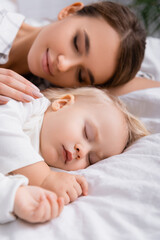 Obraz na płótnie Canvas happy mother with closed eyes touching sleeping baby boy, blurred background