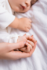 woman touching hand of little son sleeping on white bedding, blurred background
