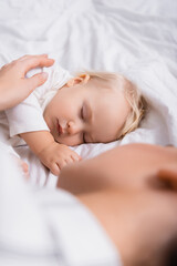 woman touching little child sleeping at home, blurred foreground
