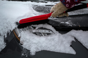 Hand of woman using brush and remove snow and ice from car and windscreen, concept of transportation and winter