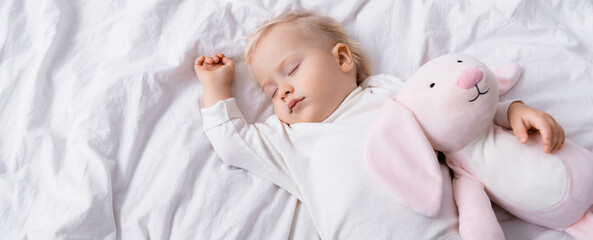 overhead view of little child sleeping with toy bunny, banner