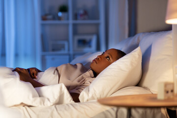 people, bedtime and rest concept - sleepless african american woman lying in bed at night and...