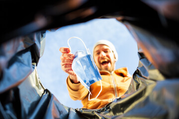 Point of view shot of happy man throwing away surgical mask in trash can	