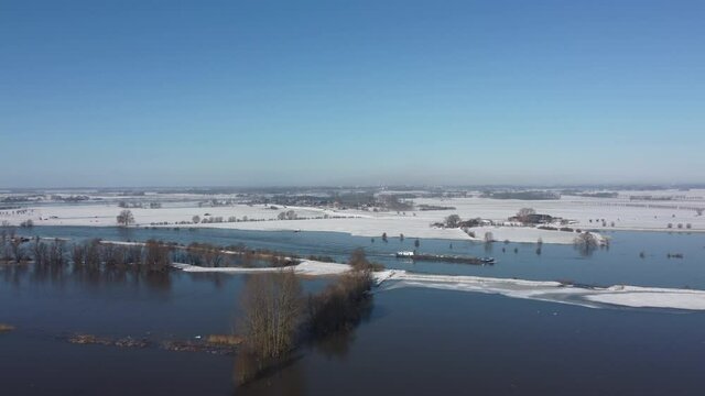 Ship on the river with high water level on the snowy floodplains of the river IJssel near the city of Zwolle in Overijssel, The Netherlands. Aerial drone point of view.