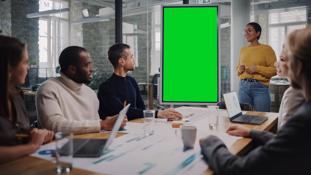 Project Manager Makes a Presentation on a Green Screen Mock Up Display for a Young Diverse Creative Team in Meeting Room in an Agency. Colleagues Sit Behind Conference Table and Discuss Business.