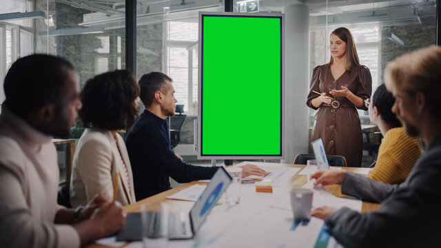 Project Manager Makes a Presentation on a Green Screen Mock Up Display for a Young Diverse Creative Team in Meeting Room in an Agency. Colleagues Sit Behind Conference Table and Discuss Business.