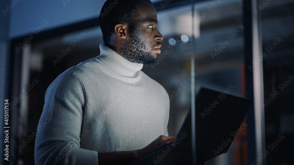 Poster handsome black african american male is standing in meeting room behind glass walls with laptop comp