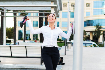 happy business woman carries shoes in her hand. A young free woman in the city.