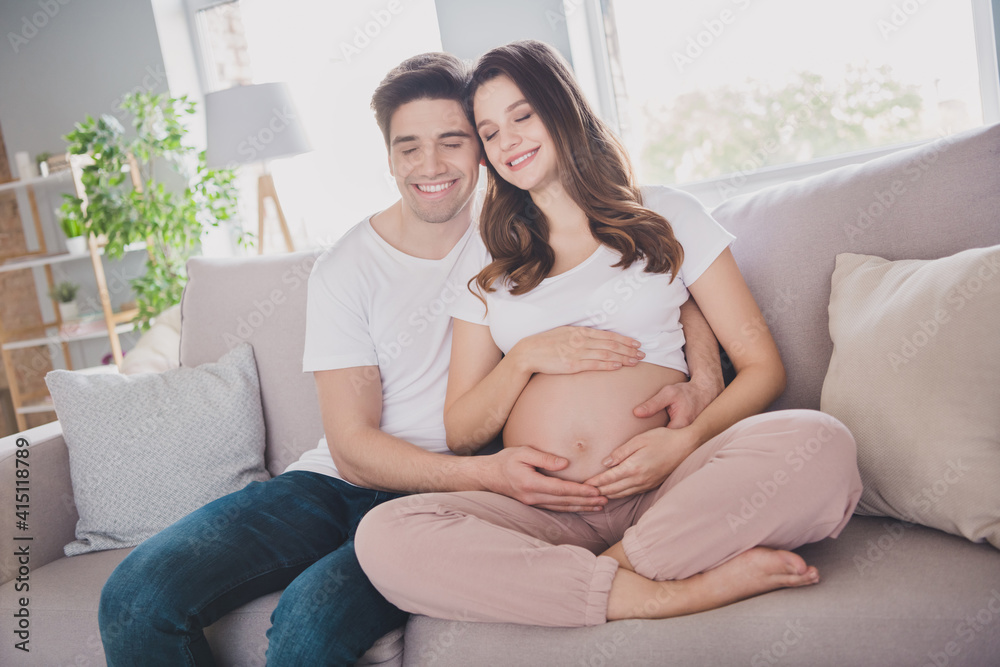 Sticker Photo of adorable cheerful funny dreamy family waiting baby sitting sofa hugging tummy closed eyes indoors inside