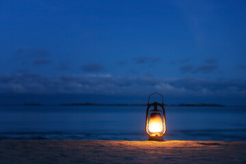 Fuel lantern on the beach close to the sea. Star sky and storm clouds above. Beach camping. Hurricane lantern. Space for text.